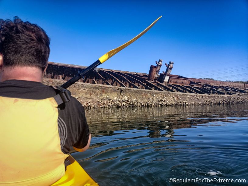 Kayaking at the Port Adelaide ships' graveyard next to the barnacle-covered ruins of the abandoned Santiago shipwreck under a bright blue sky.